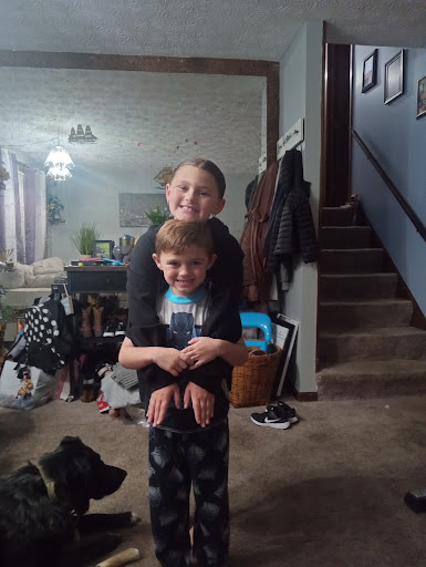 Two children having fun together at home, with one giving the other a piggyback ride while a dog observes.