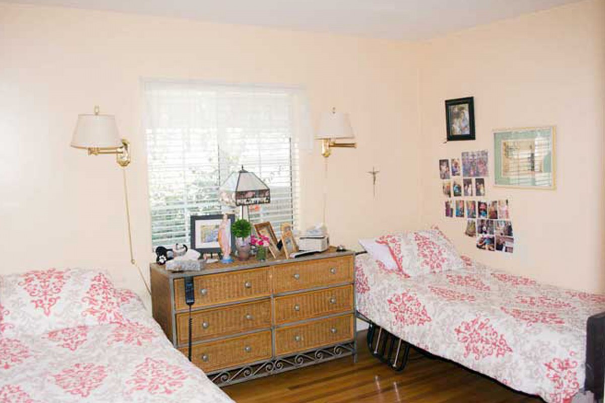 A cozy bedroom featuring twin beds with matching floral bedding, a dresser between them adorned with decor, and photos displayed on the wall.