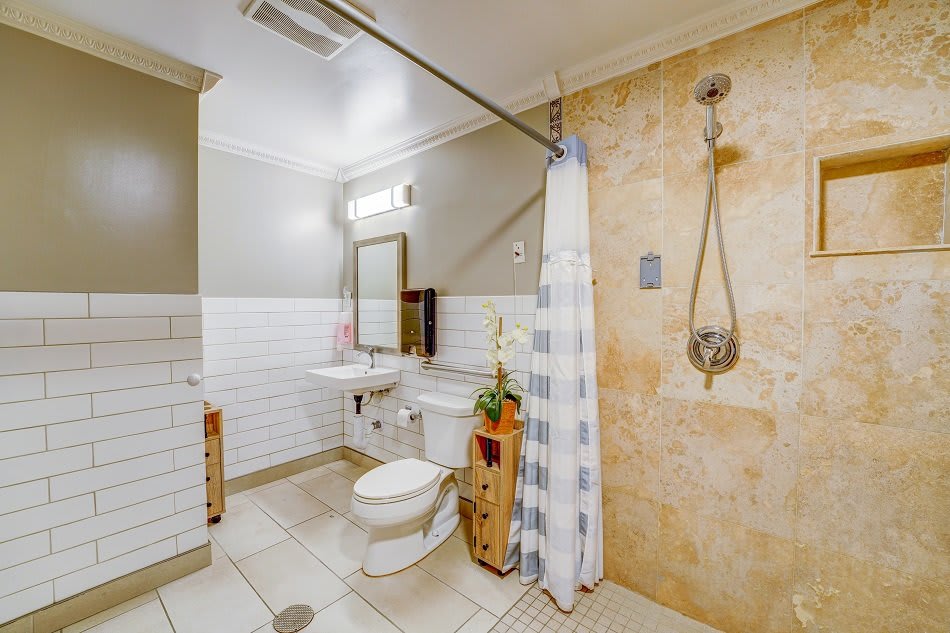 A well-lit bathroom featuring a shower with a curtain, toilet, sink, and mirror.