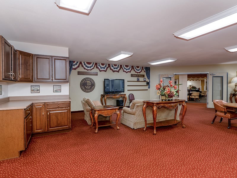 A cozy living room with a seating area, television, and decorative elements on a red carpeted floor.