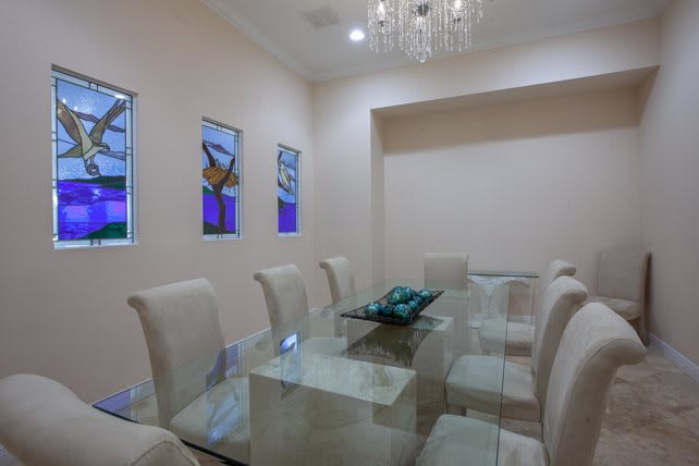 A modern dining room featuring a glass table surrounded by upholstered chairs, complemented by a chandelier and contemporary artwork on the walls.