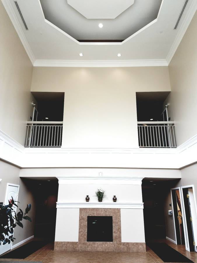A modern living room with a high ceiling and balcony overlooking a central fireplace.