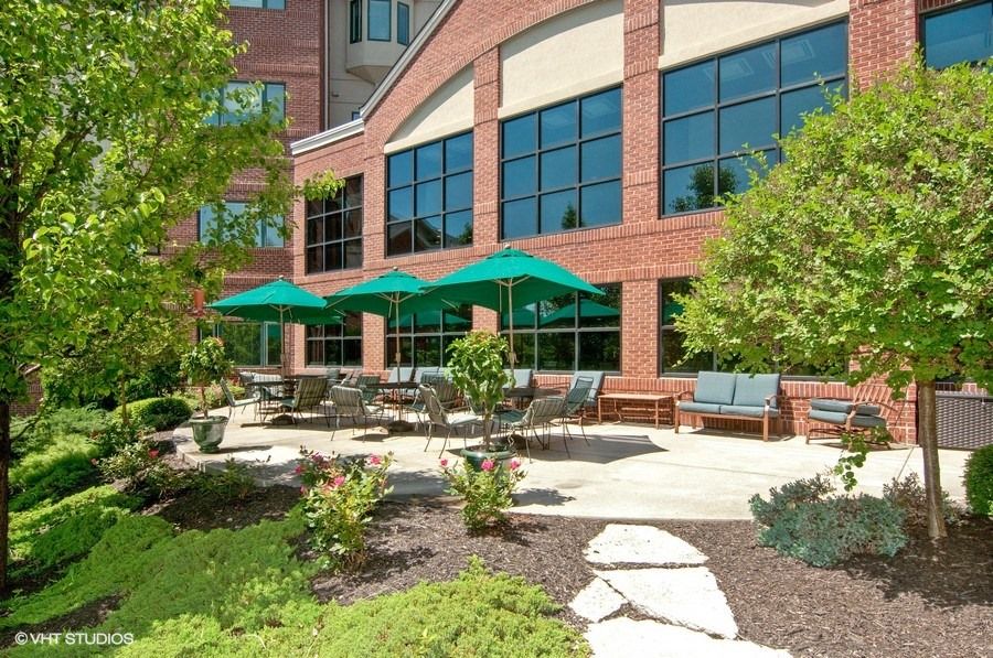 A modern building with a landscaped outdoor patio featuring seating and green umbrellas.