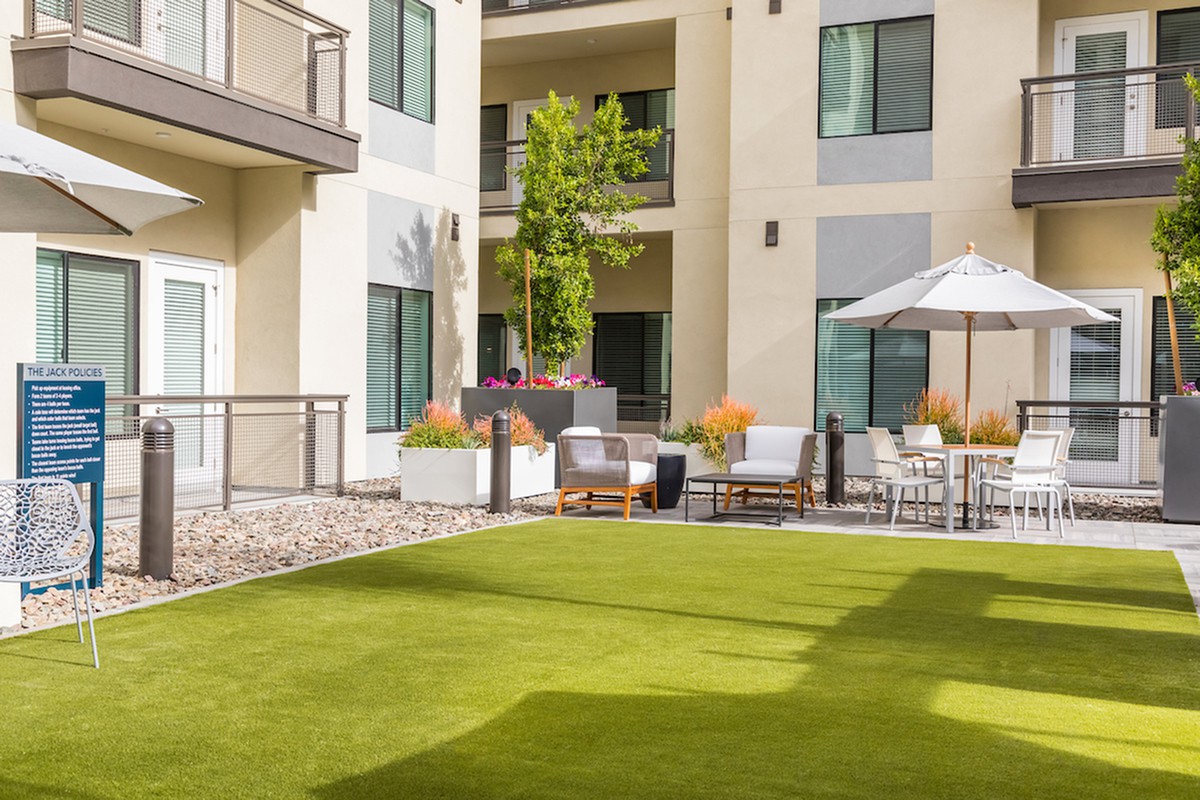 A modern apartment courtyard with a well-manicured lawn and outdoor seating area.