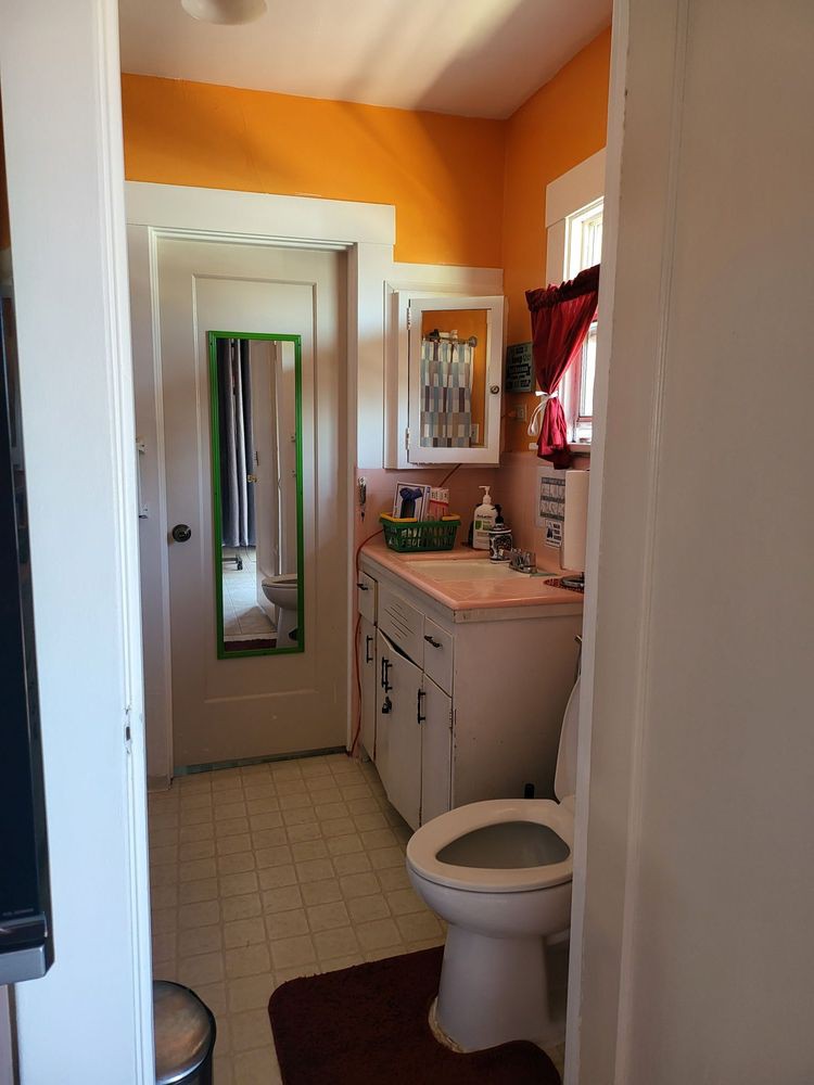 A small bathroom with orange walls, featuring a mirror, sink, and toilet.