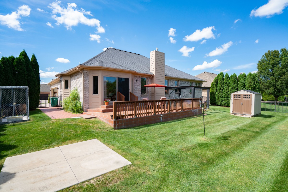 A suburban house with a spacious backyard, featuring a wooden deck and patio furniture on a sunny day.