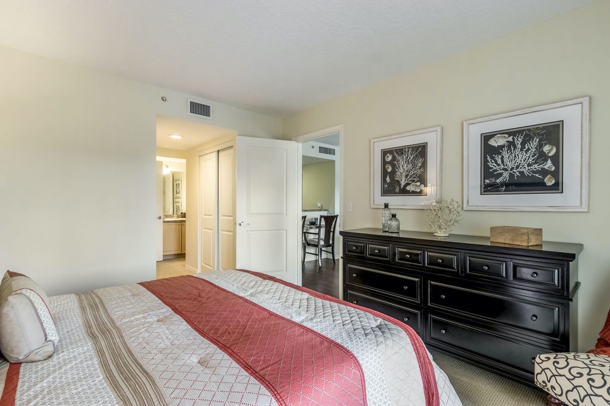 A cozy bedroom with a neatly made bed, a dark dresser, and framed artwork on the walls.