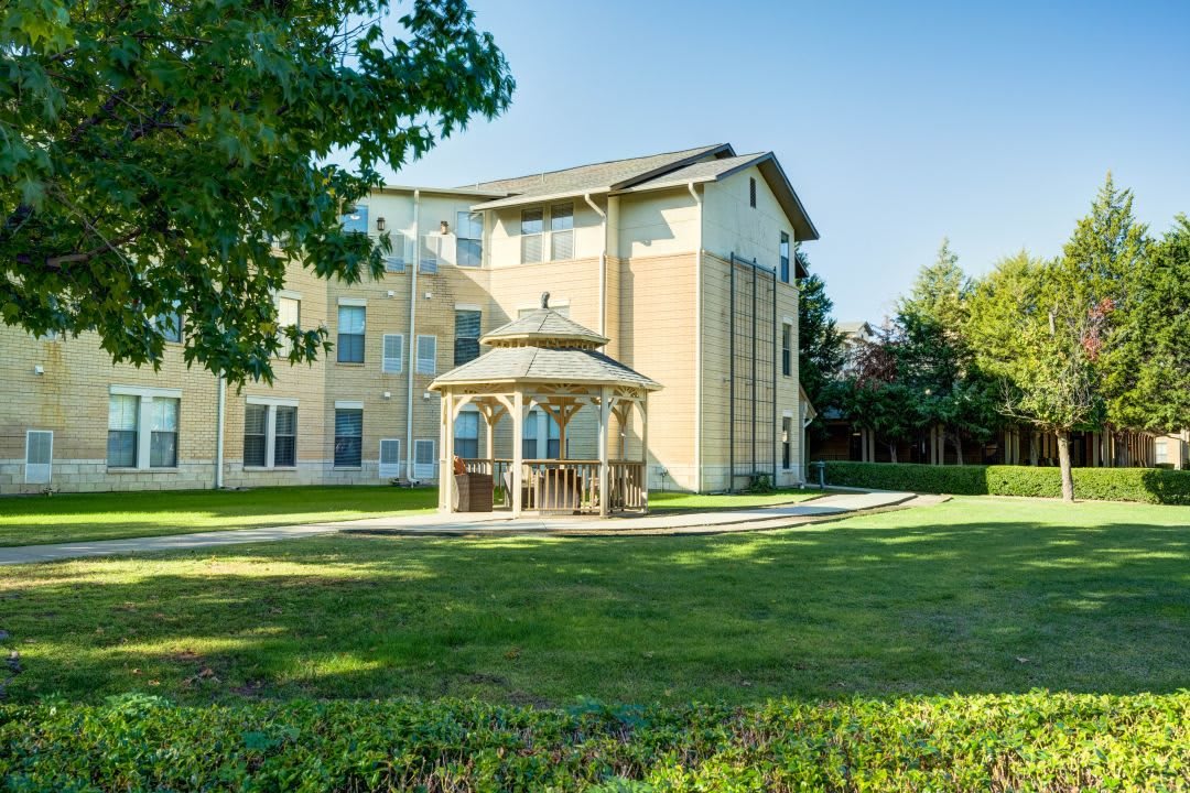 A three-story building with a gazebo on a well-maintained lawn surrounded by trees.