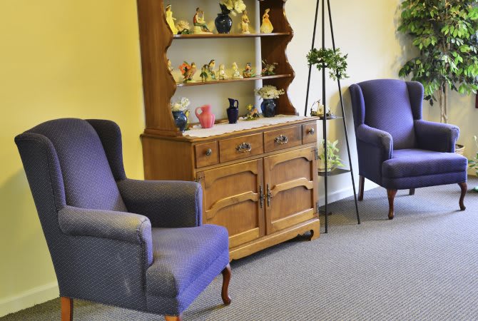 A cozy living room with purple armchairs and a wooden cabinet displaying decorative items.