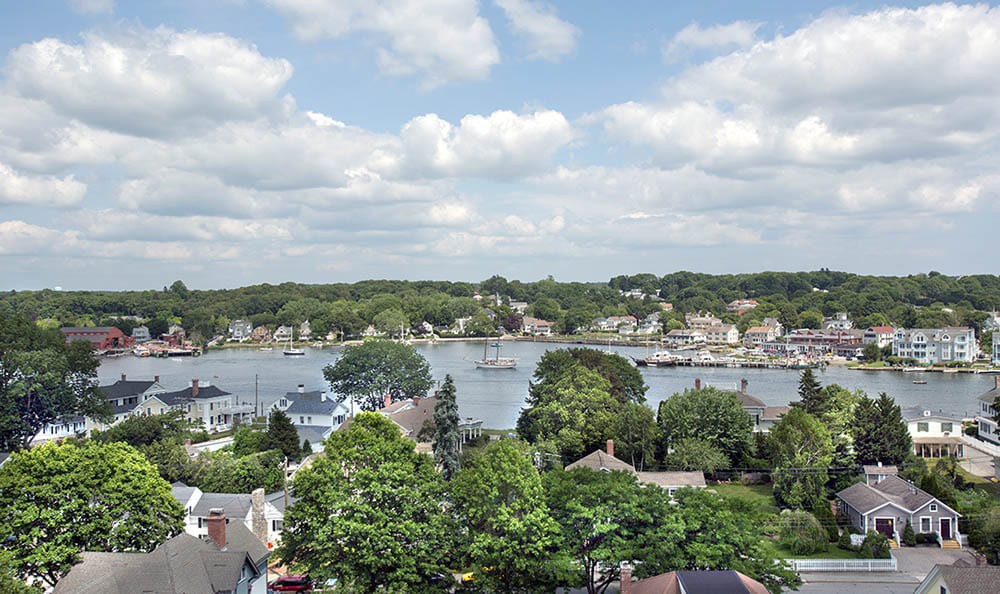 A scenic view of a riverside town with lush greenery and scattered clouds in the sky.