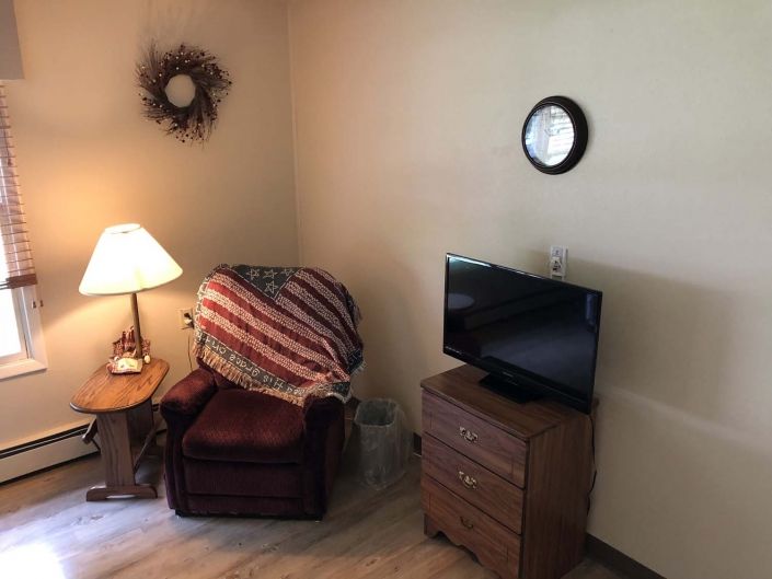 A cozy living room corner with a chair, lamp, TV, and wall decorations.