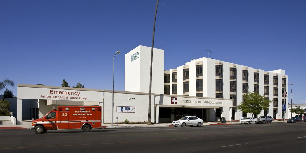 A view of a hospital building with an emergency vehicle parked outside on a clear day.