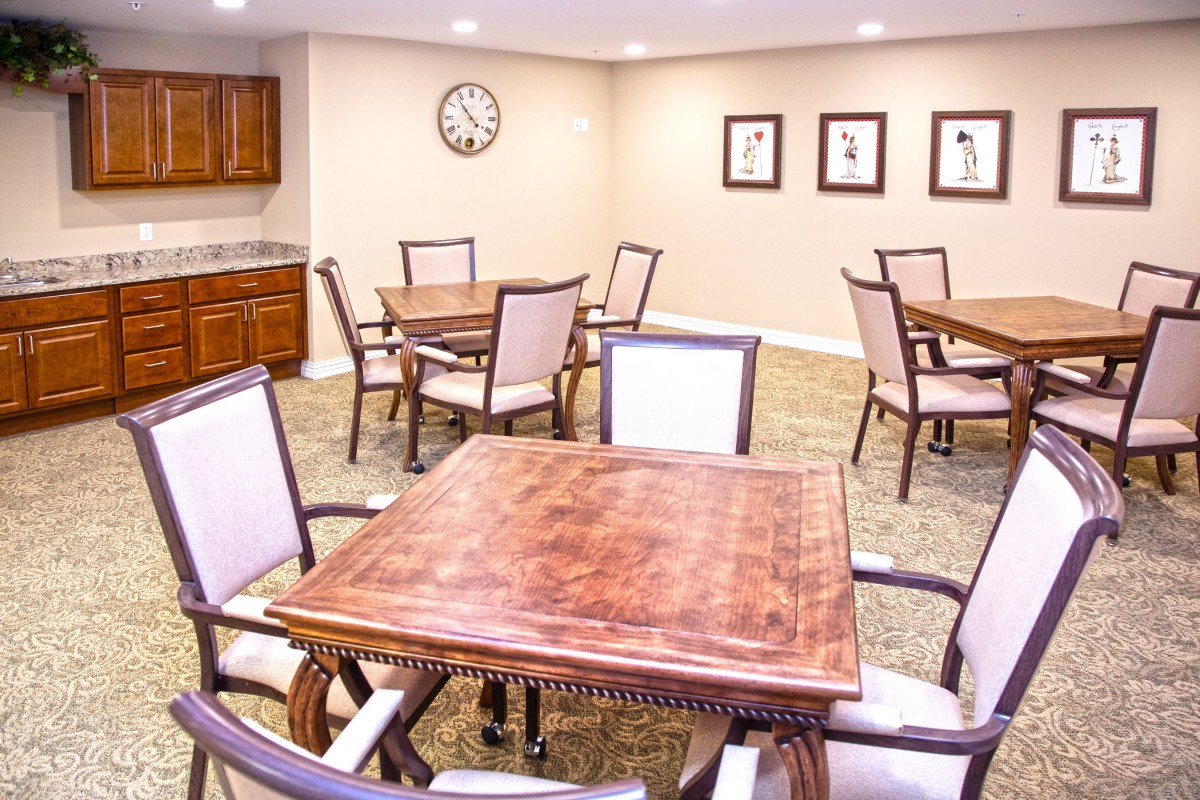 A cozy dining room with multiple wooden tables and upholstered chairs, featuring wall artwork and a clock.
