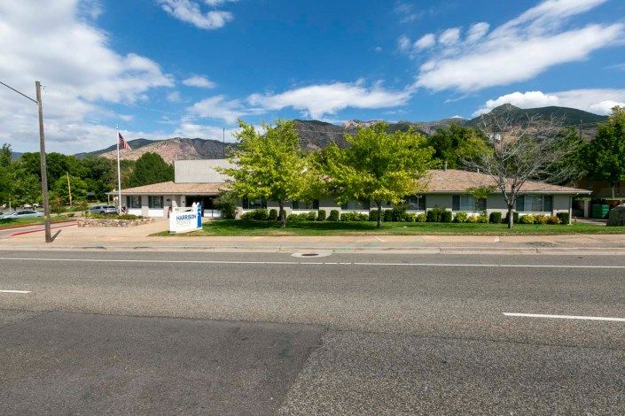 A roadside building surrounded by trees and mountains under a bright blue sky with clouds.