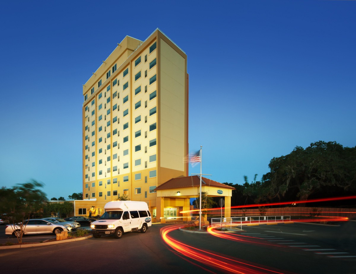 A tall hotel building illuminated at night with vehicles in the parking area.