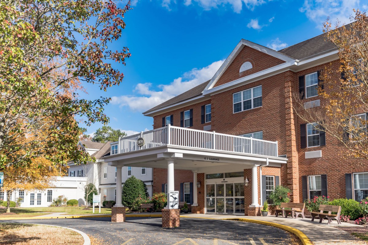 A sunny day at a brick residential building with a prominent entrance and balcony.