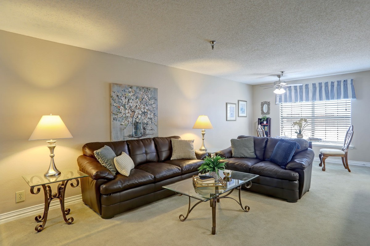 A cozy living room with two sofas, a glass coffee table, lamps, and artwork on the wall.