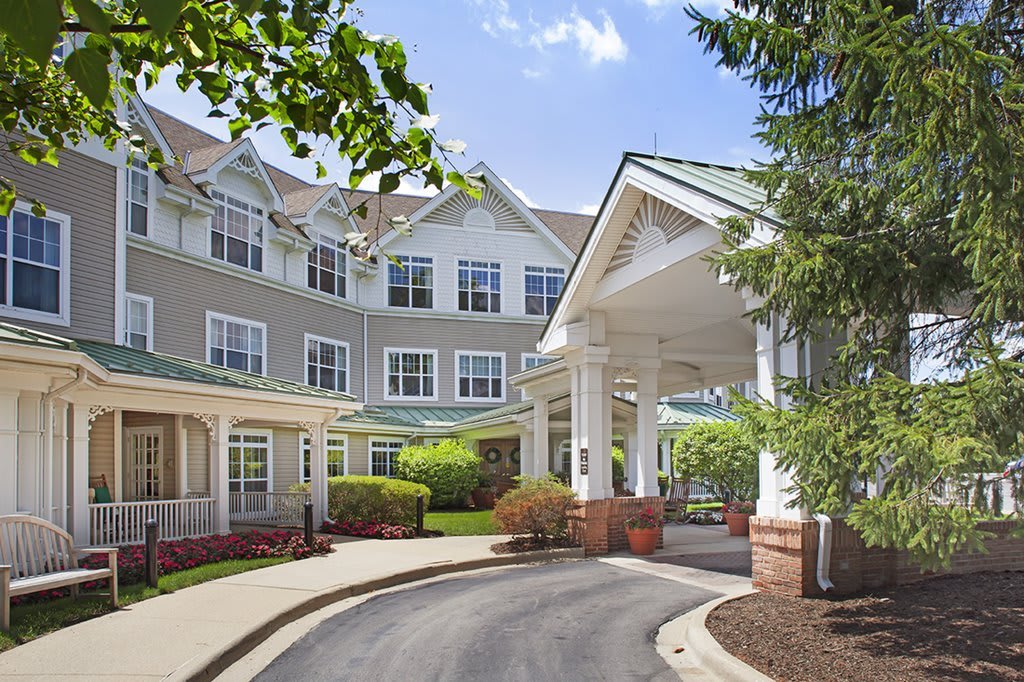 A picturesque entrance of a residential building with a landscaped driveway and surrounding greenery.