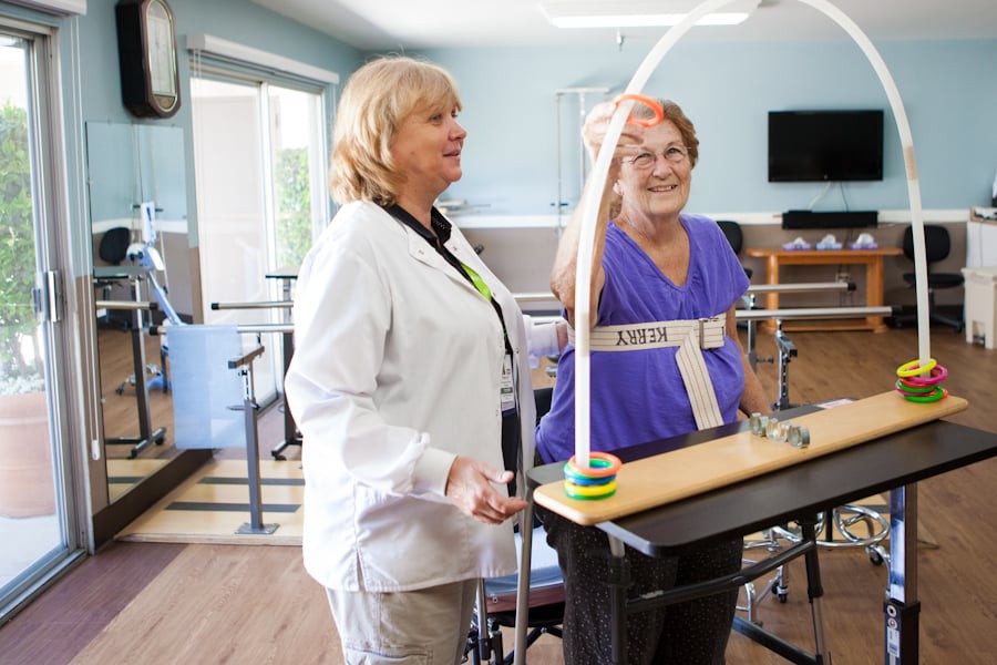 A healthcare professional assists an elderly woman during a physical therapy session focused on balance training.
