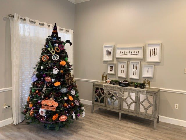 A creatively decorated Christmas tree with a Halloween theme, featuring pumpkins and a witch hat in a cozy interior.