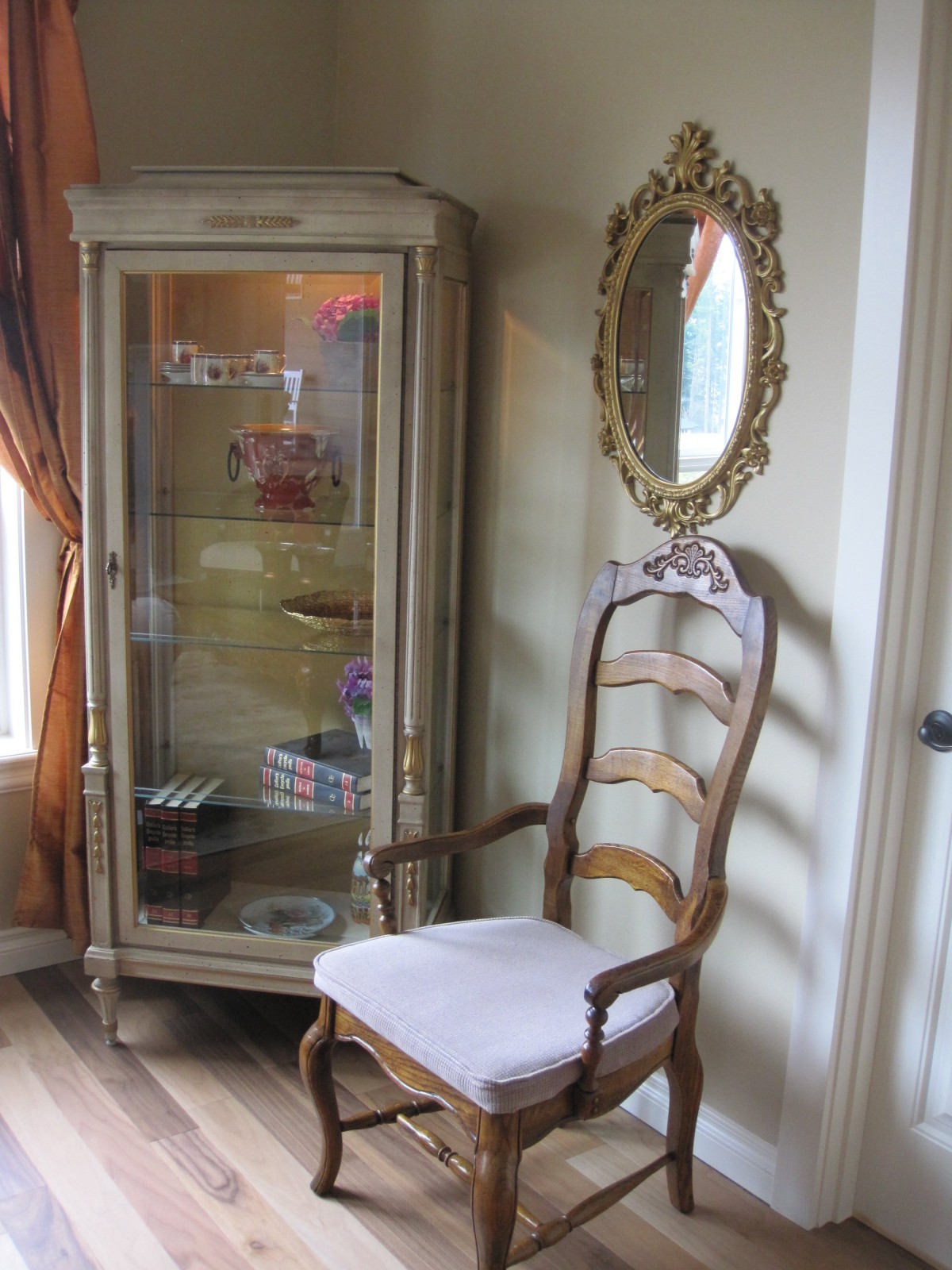 A vintage room corner with an antique chair, a glass display cabinet, and an ornate mirror.
