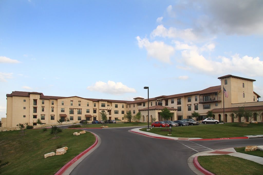 A large residential building with a circular driveway and landscaped surroundings under a partly cloudy sky.