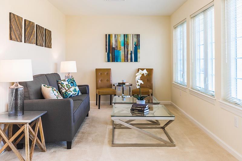 A modern living room with a sofa, two chairs, a glass coffee table, and decorative artwork on the wall.