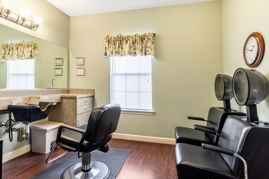 A well-lit hair salon interior featuring chairs, a mirror, and a window with light streaming in.