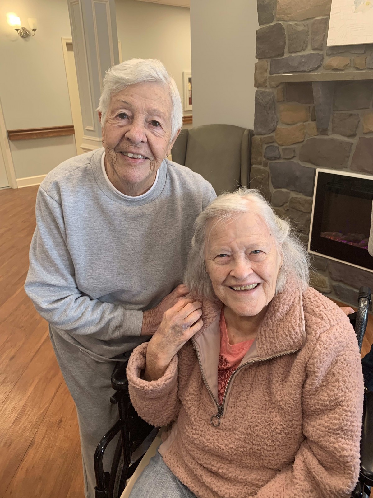 Two elderly women smiling together indoors.