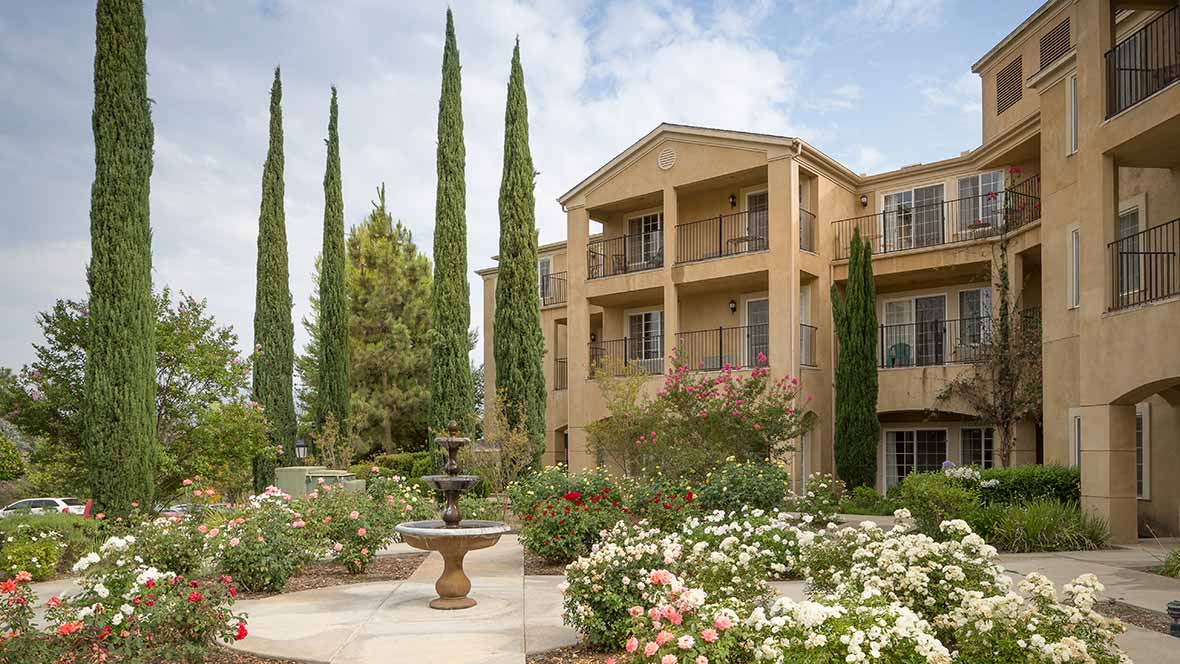 A well-landscaped apartment complex with a fountain and tall trees.
