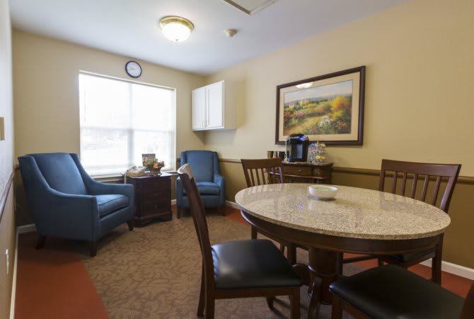 A cozy living room with a round table, chairs, and armchairs by the window.