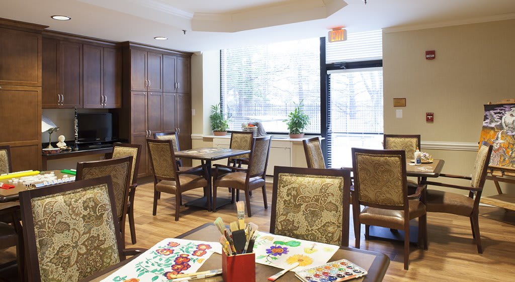 A bright art room with tables and chairs, featuring paintings and brushes on the table.