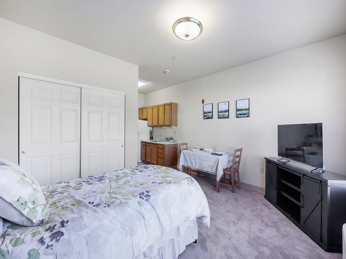 A cozy studio apartment featuring a combined sleeping and living area with a small kitchenette and dining table.