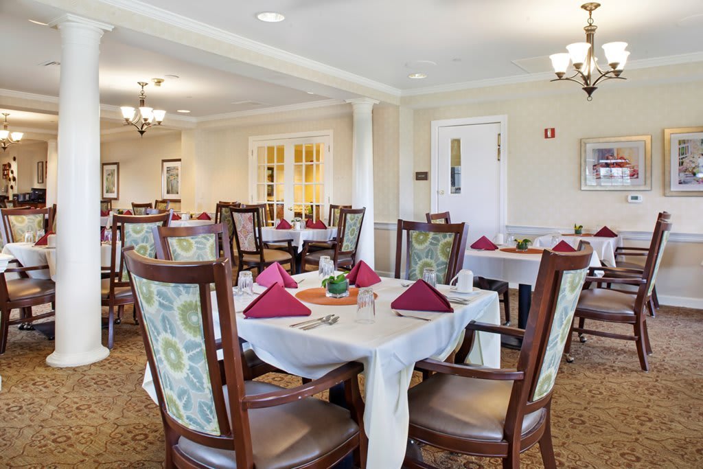 A well-decorated dining room with neatly arranged tables and chairs, featuring elegant place settings and ambient lighting.