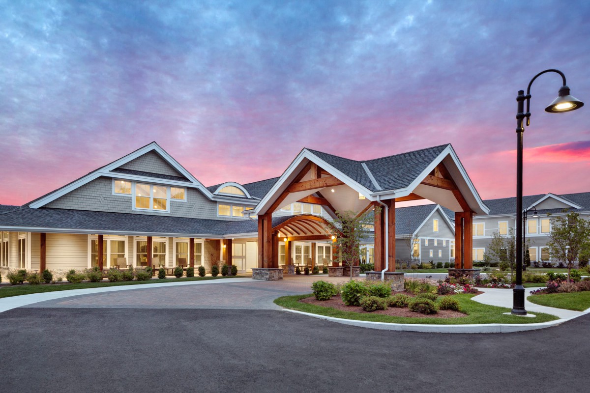 A beautifully designed residential building with a spacious driveway, set against a vibrant sunset sky.