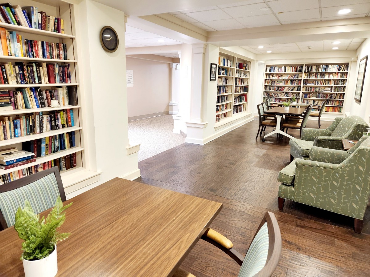 A cozy library space with bookshelves, tables, and chairs for reading.