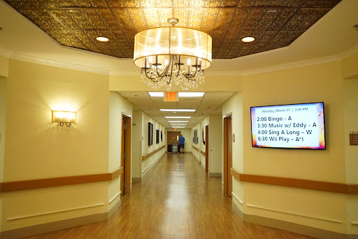A well-lit hospital hallway featuring a chandelier and artwork along the walls.