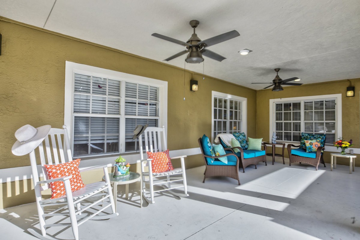 A cozy patio area featuring rocking chairs, colorful cushions, and ceiling fans.