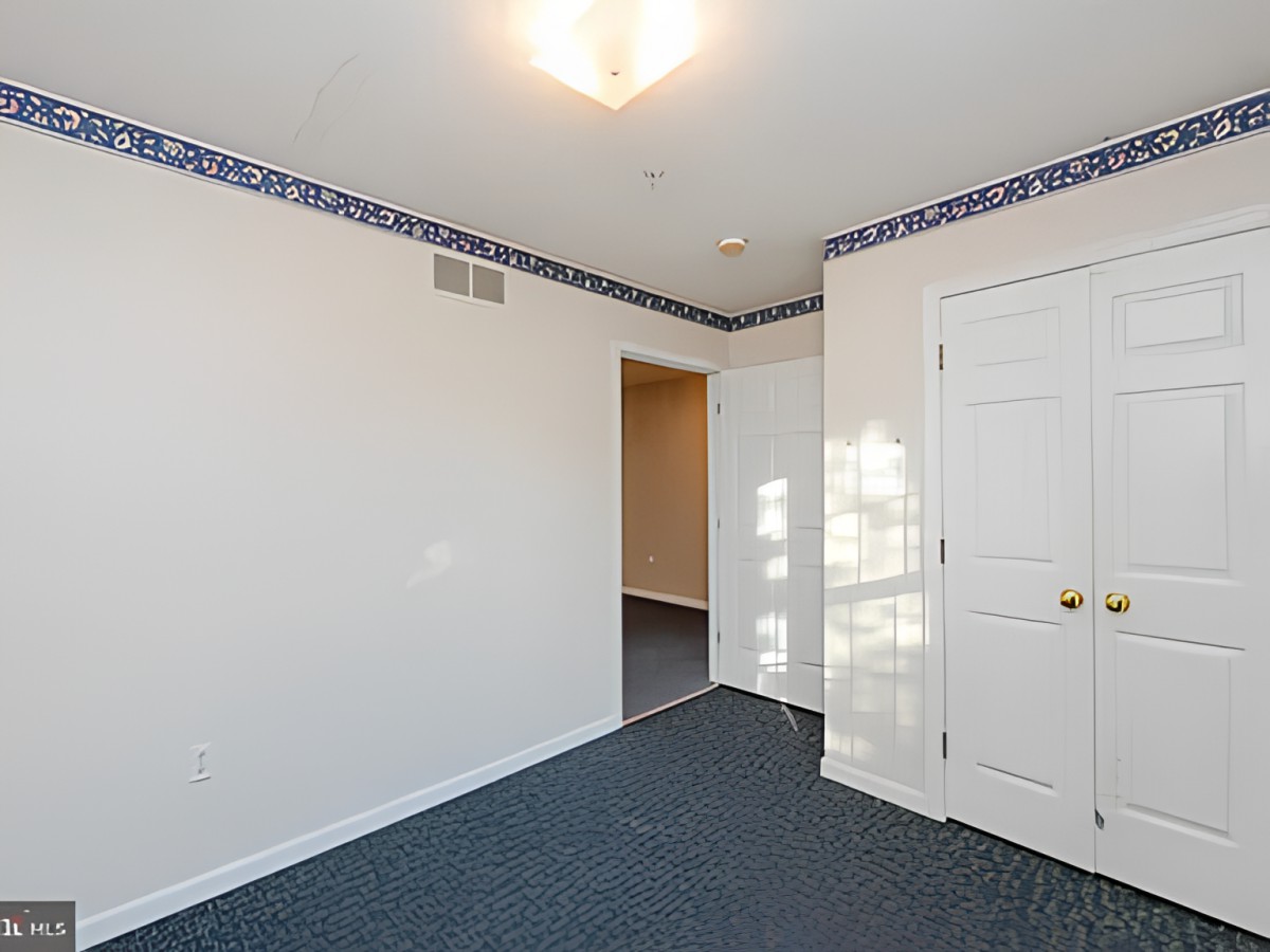 An empty room with white walls, a blue carpeted floor, and a ceiling light.