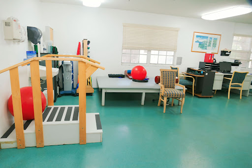 A well-equipped physical therapy room featuring exercise machines, balls, and a comfortable seating area.