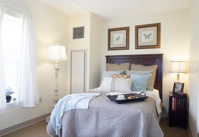A cozy and well-decorated bedroom with a neatly made bed, pillows, wall art, and a standing lamp.