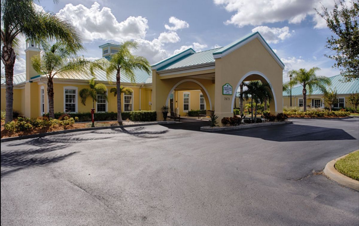 A tropical-style hotel entrance with palm trees under a sunny sky.