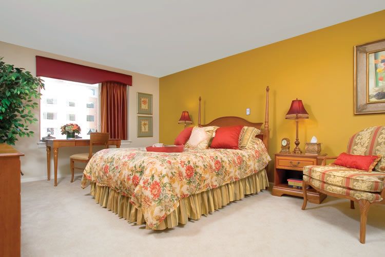 A cozy bedroom with a yellow accent wall, floral bedding, and warm lighting.