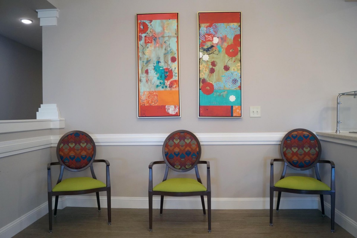 A waiting room with three chairs and colorful abstract artwork on the wall.