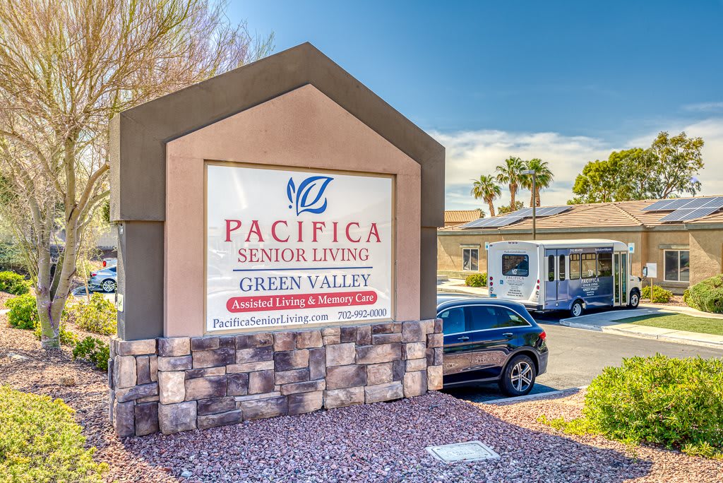 A sign for Pacifica Senior Living Green Valley, located outdoors with a vehicle parked nearby.