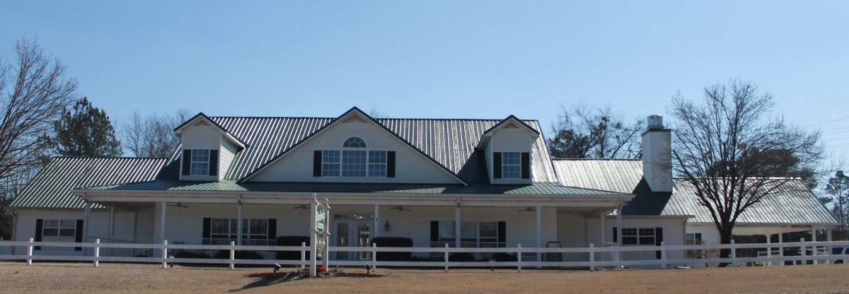 A two-story house with a metal roof and a front porch, surrounded by a white fence.