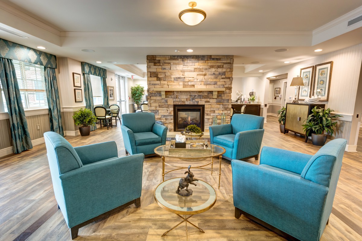 A cozy living room featuring blue armchairs arranged around a glass coffee table, with a stone fireplace as the focal point.