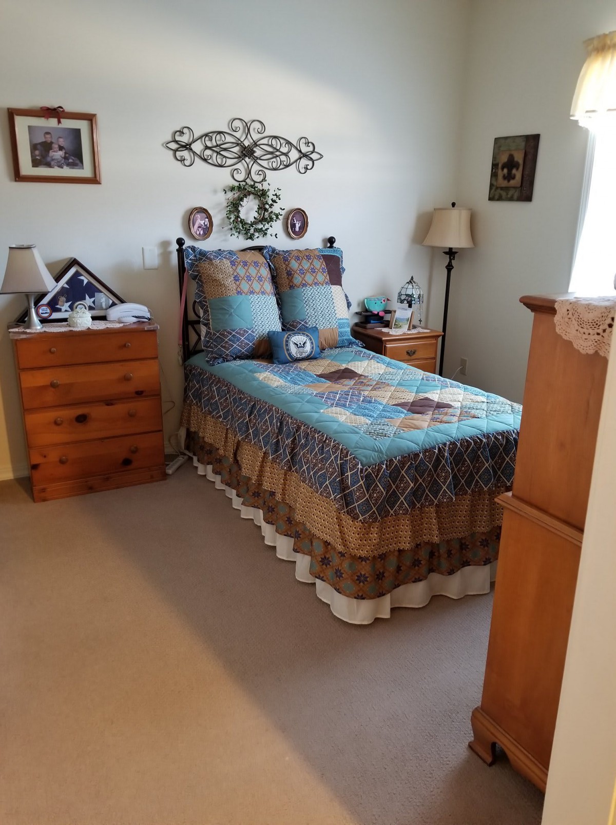 A cozy bedroom with a neatly made bed, adorned with a patchwork quilt. Wooden nightstands flank the bed, topped with lamps and decor. Wall art adds a personal touch to the room.
