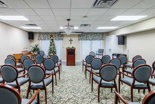 A serene interior setting with rows of chairs facing a podium, featuring a decorative tree and a religious symbol.
