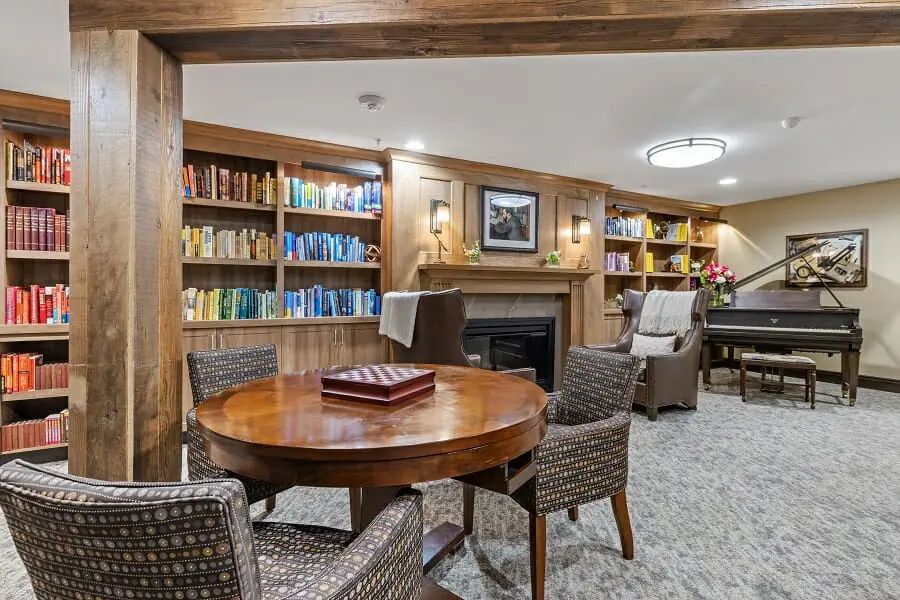 A cozy library room with bookshelves, a fireplace, and comfortable seating.